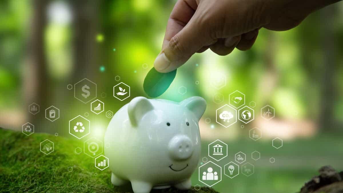 Hand putting a leaf in a piggy bank with a green outdoor background and environment related icons.