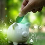 Hand putting a leaf in a piggy bank with a green outdoor background and environment related icons.