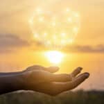 aHands pretending to hold the sun with a graphic love heart on top.