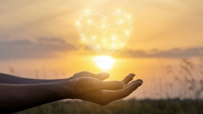 aHands pretending to hold the sun with a graphic love heart on top.