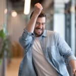 Ecstatic man giving a fist pump in an office hallway.