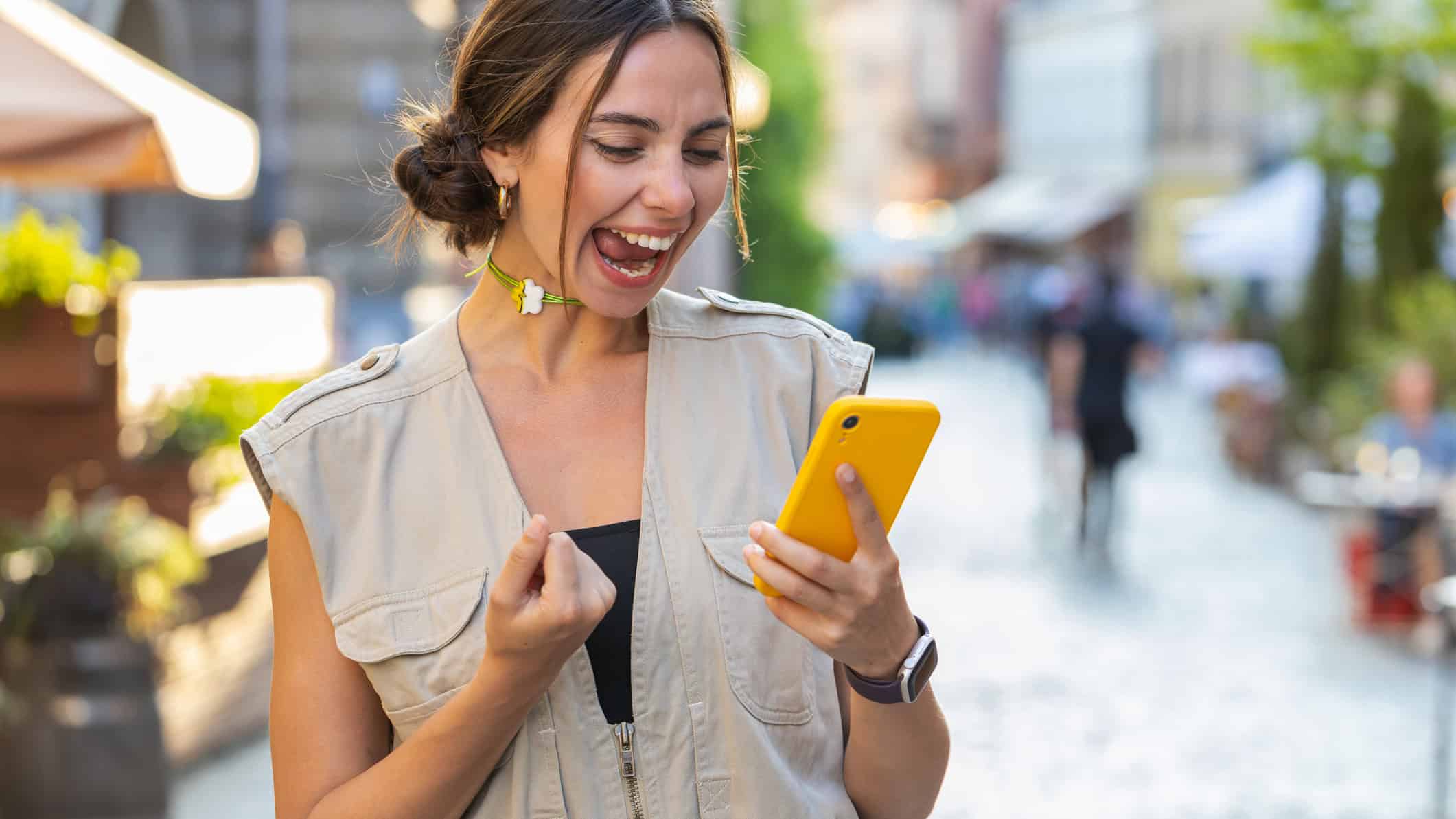 Ecstatic woman looking at her phone outside with her fist pumped.