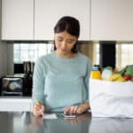 Latin American woman at home checking her budget after grocery shopping.