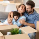 Happy mum and dad with daughter smiling on couch after relocation to new home.