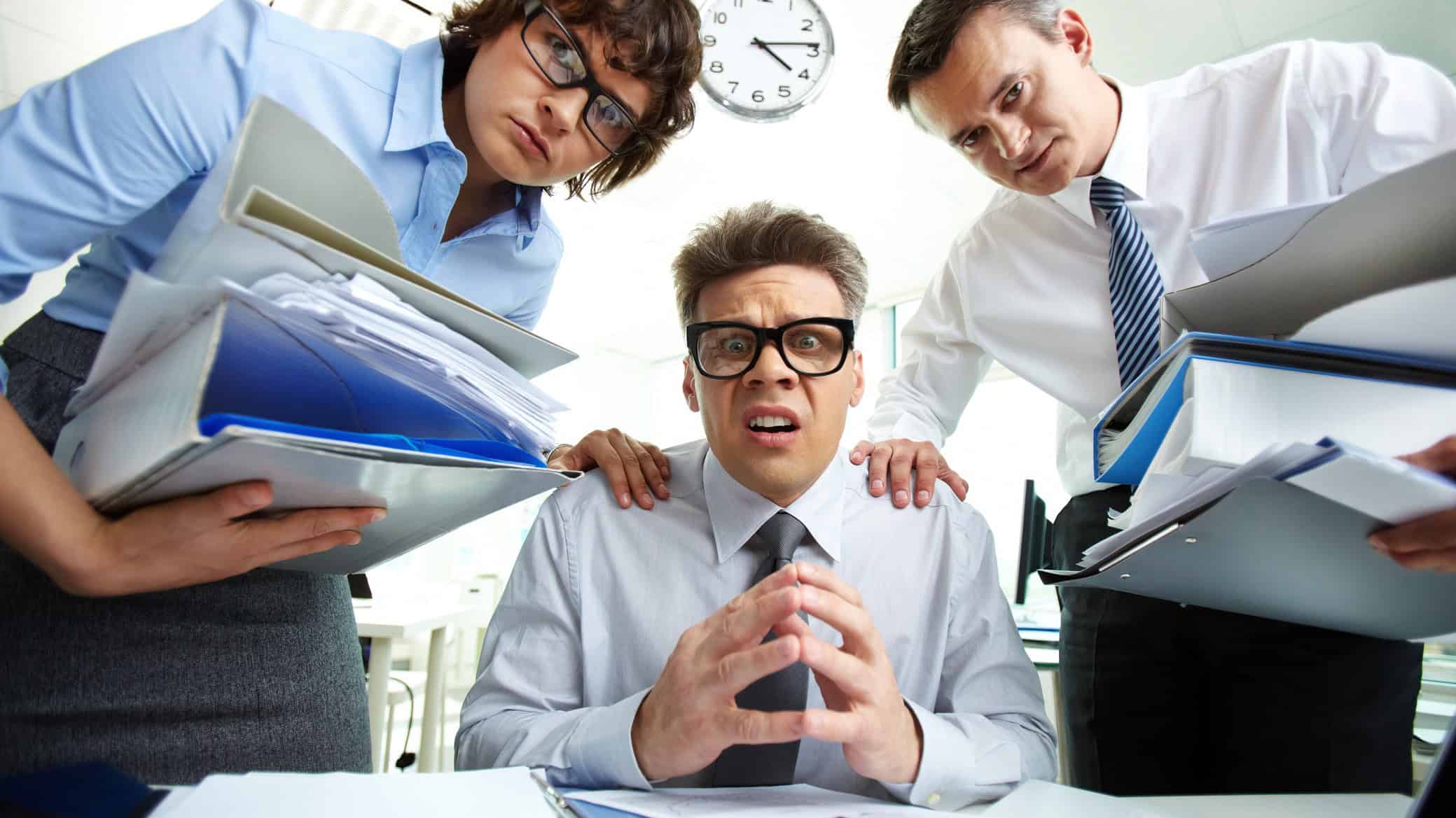 Three business people look stressed as they contemplate stacks of extra paperwork.