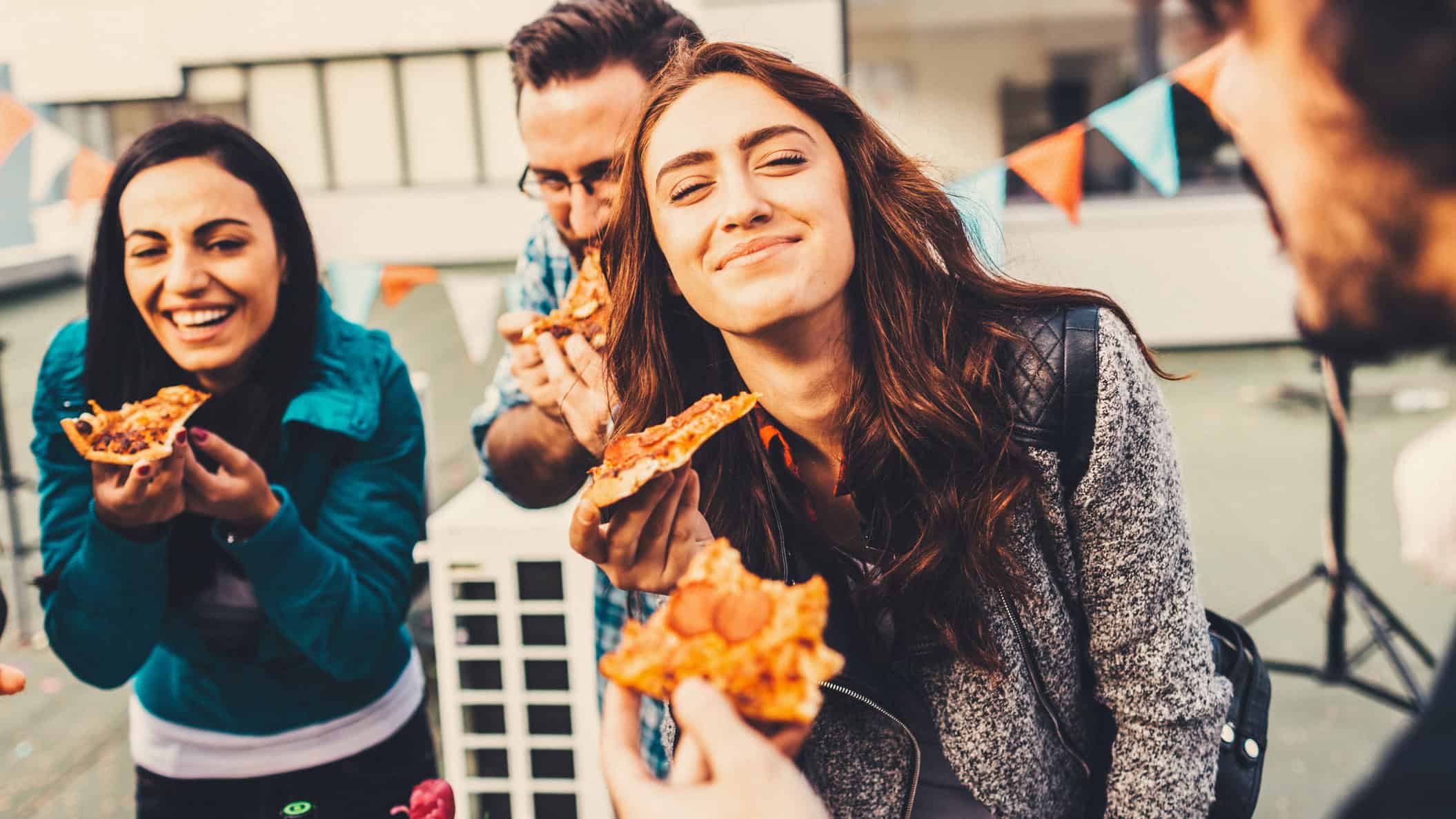 Happy friends at a party enjoying pizza, symbolising the Domino's Pizza share price.