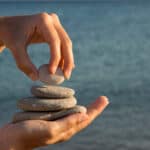 Person stacking rocks in their hand with water in the background.