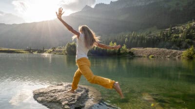 Woman stepping on big rock in a lake.