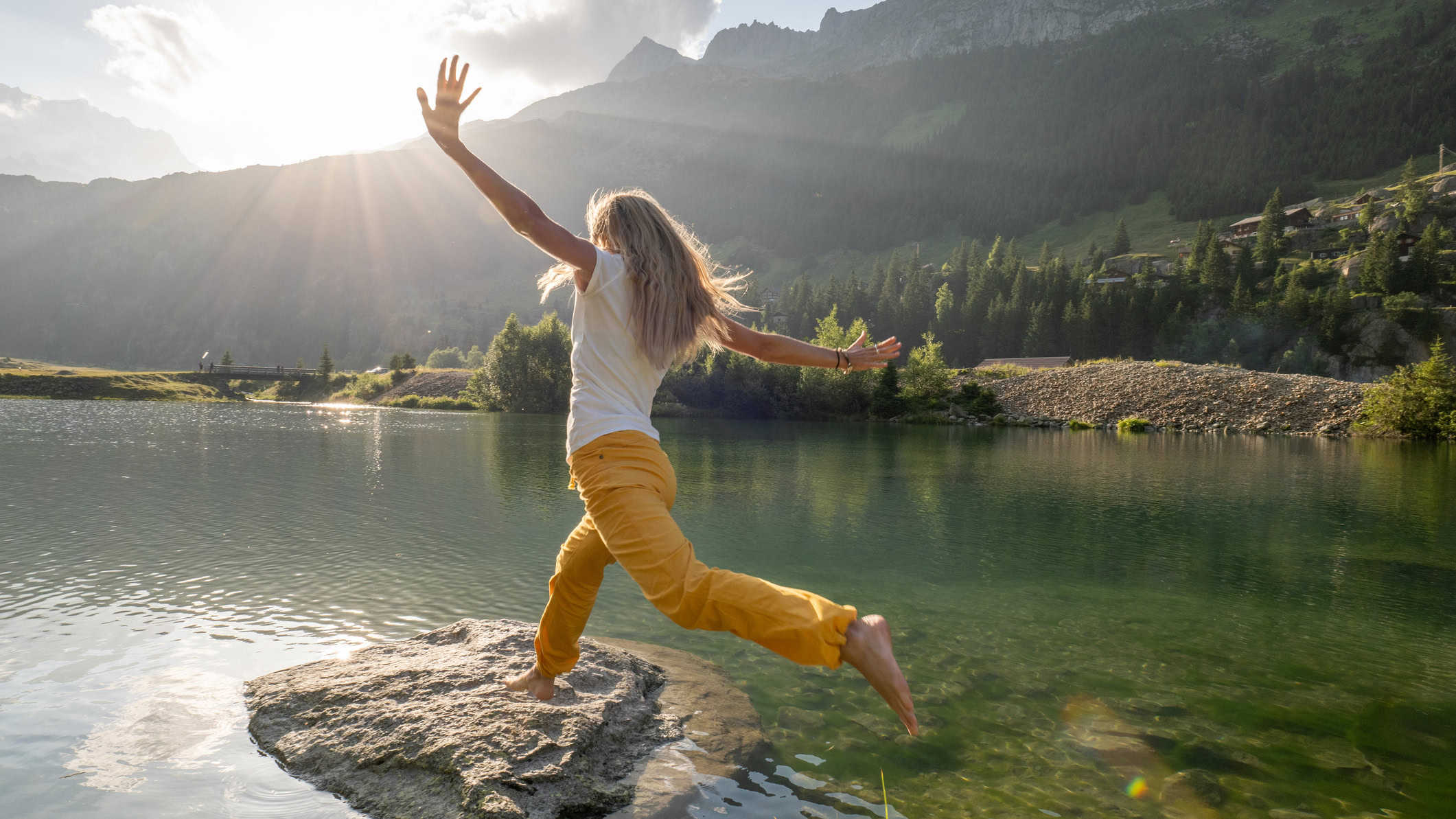 Woman stepping on big rock in a lake.