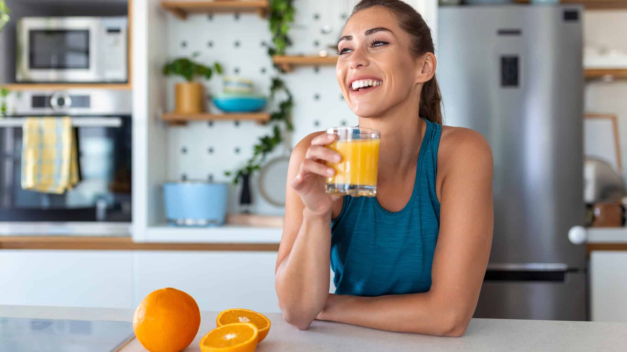 Beautiful young woman drinking fresh orange juice in kitchen.