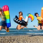 Three happy girls on jumping motion with inflatable mattresses at the beach.