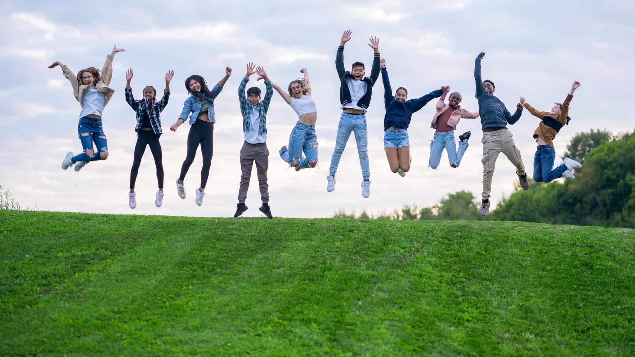 Ten happy friends leaping in the air outdoors.