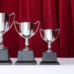 Three trophies in declining sizes with a red curtain backdrop