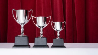 Three trophies in declining sizes with a red curtain backdrop