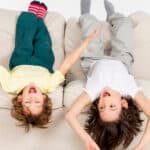 Siblings laying upside down on a couch.