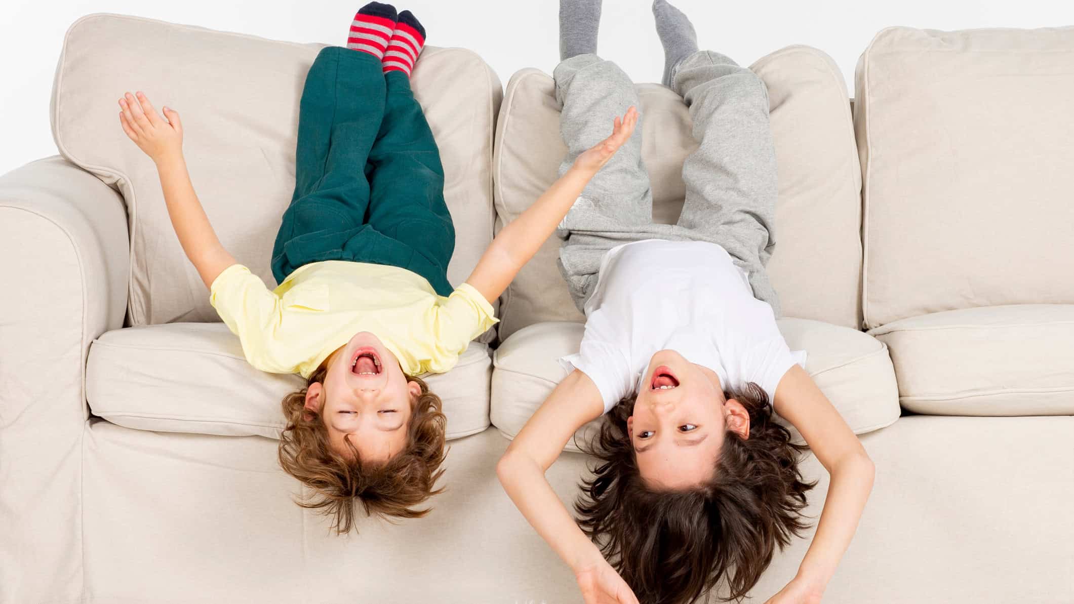 Siblings laying upside down on a couch.
