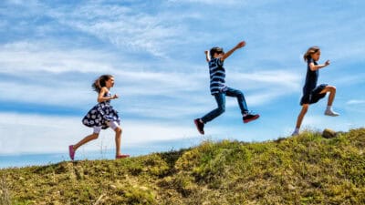 Children skipping and jumping up a hill.