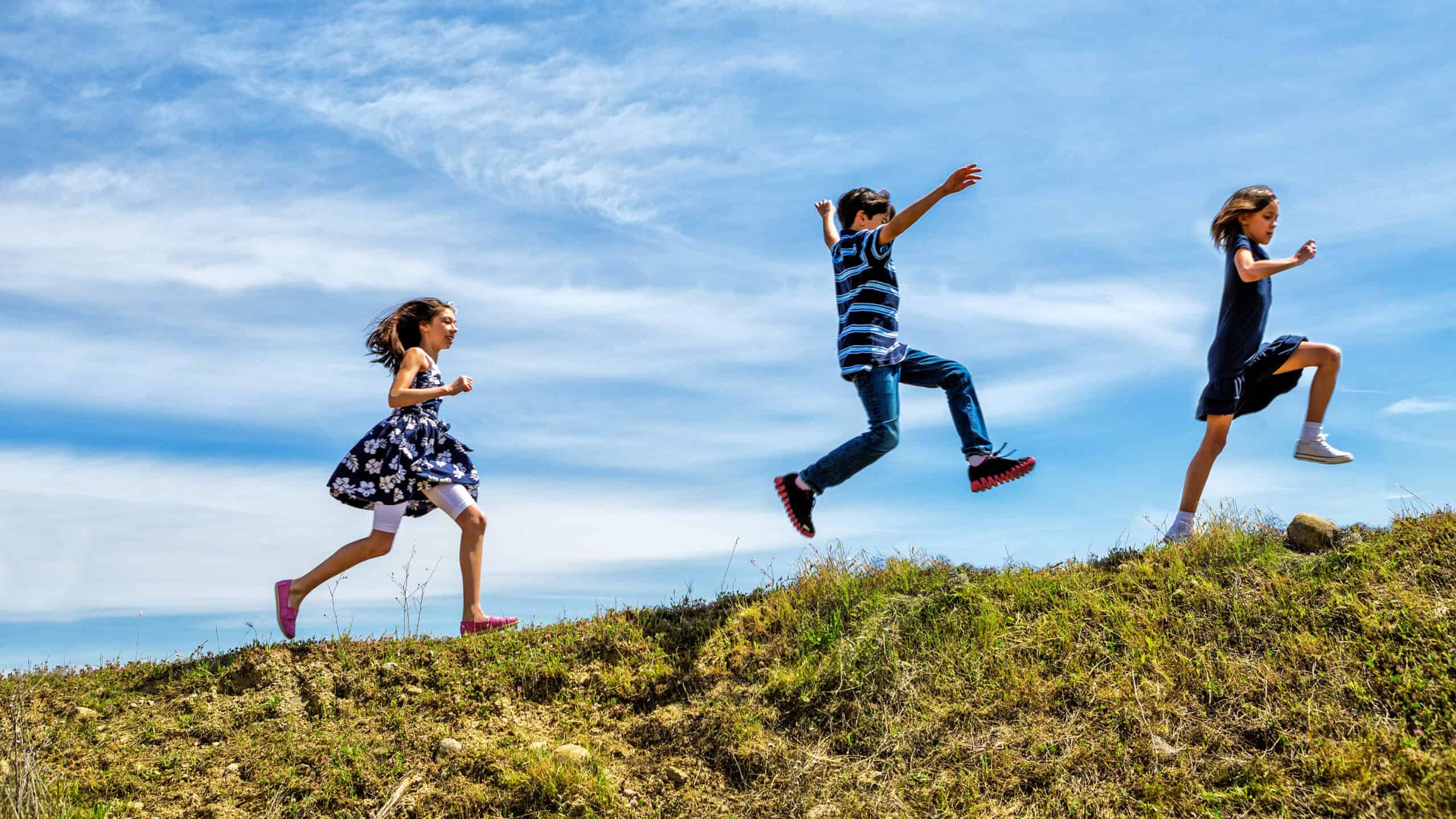 Children skipping and jumping up a hill.