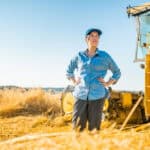 Woman standing in a wheat farm with a tractor.