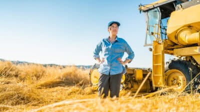 Woman standing in a wheat farm with a tractor.