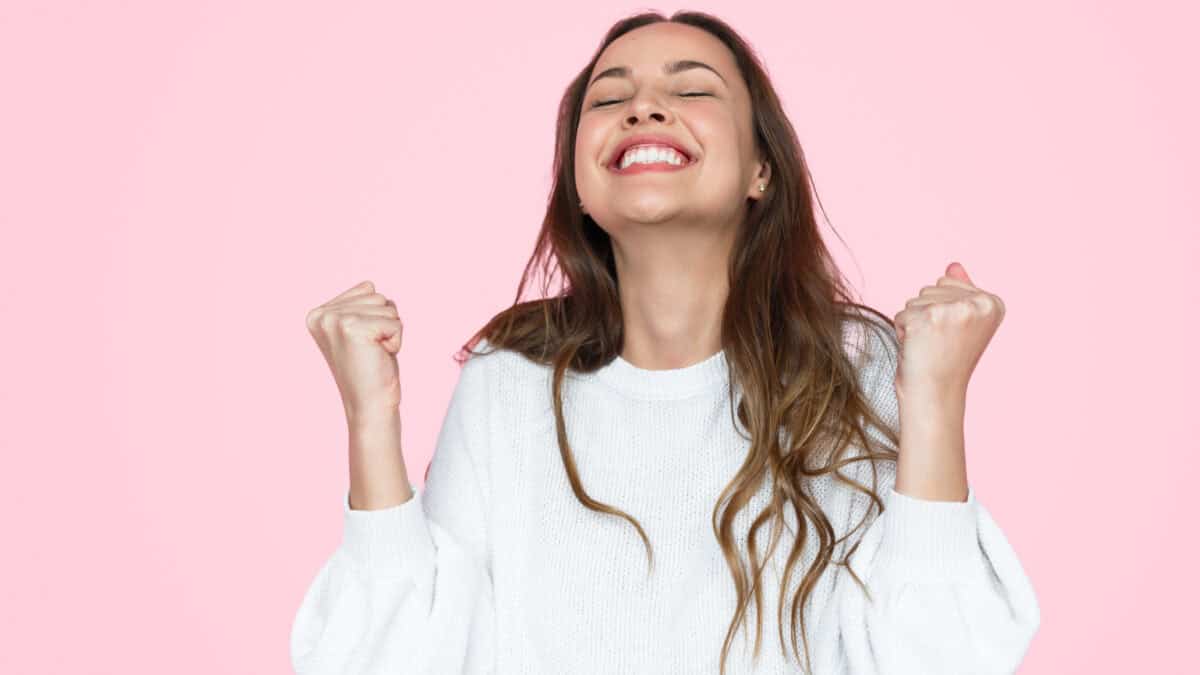 Female in elegant outfit smiling and gesturing victory with hands.