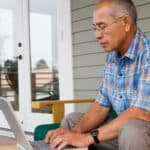 Retiree using a laptop outside his house.