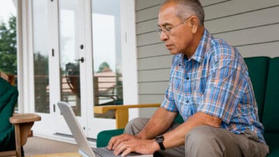 Retiree using a laptop outside his house.
