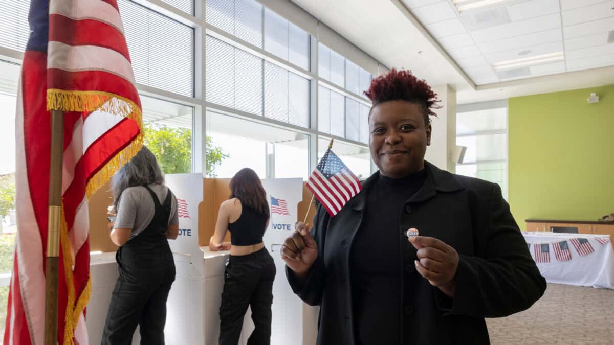 Happy voter holding the US flag and a badge.