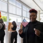 Happy voter holding the US flag and a badge.