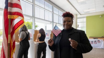 Happy voter holding the US flag and a badge.
