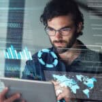 Man working on his tablet with hologram of a world map and financial-related charts.