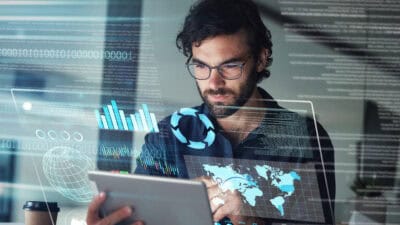 Man working on his tablet with hologram of a world map and financial-related charts.