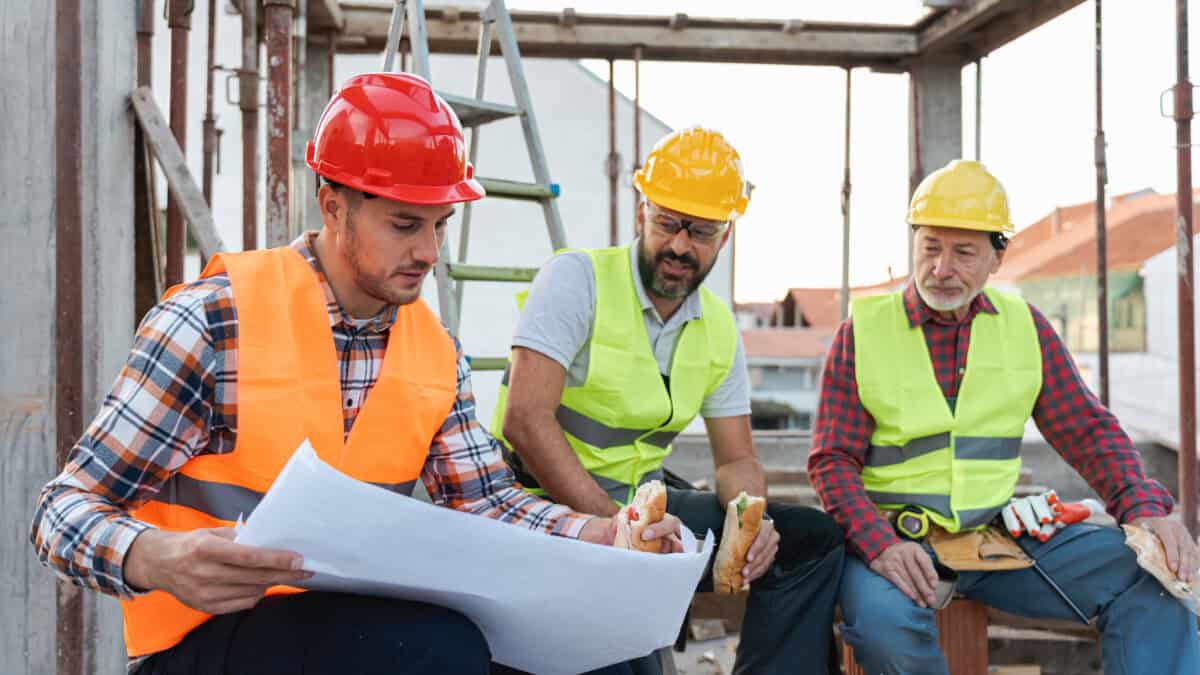 Three people at a building site discussing a plan whilst eating.