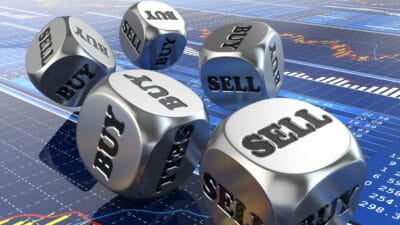 Silver dice with buy and sell written on them on top of stock market charts.