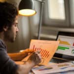 Man analysing a stock market chart, with more data on his laptop and table.