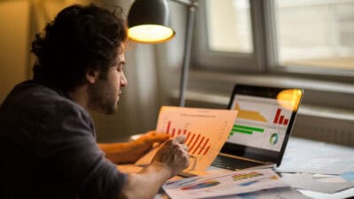 Man analysing a stock market chart, with more data on his laptop and table.