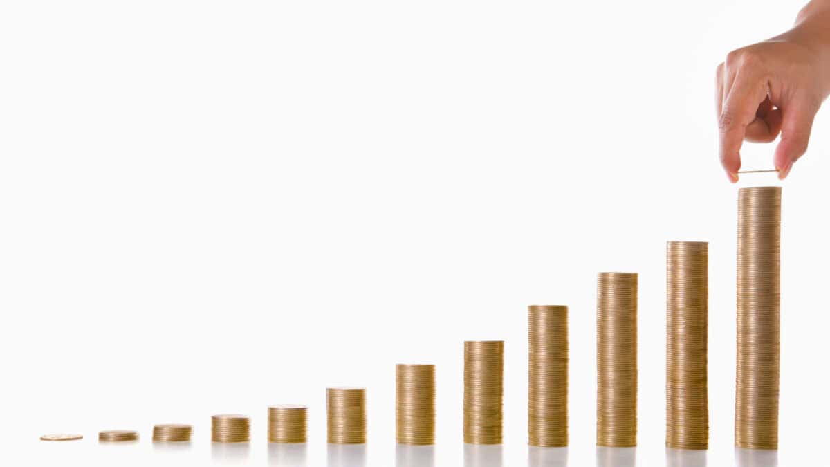 A hand is adding more coins to the highest stack, with twelve stacks of coins showing growth every month for a year.