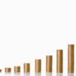 A hand is adding more coins to the highest stack, with twelve stacks of coins showing growth every month for a year.