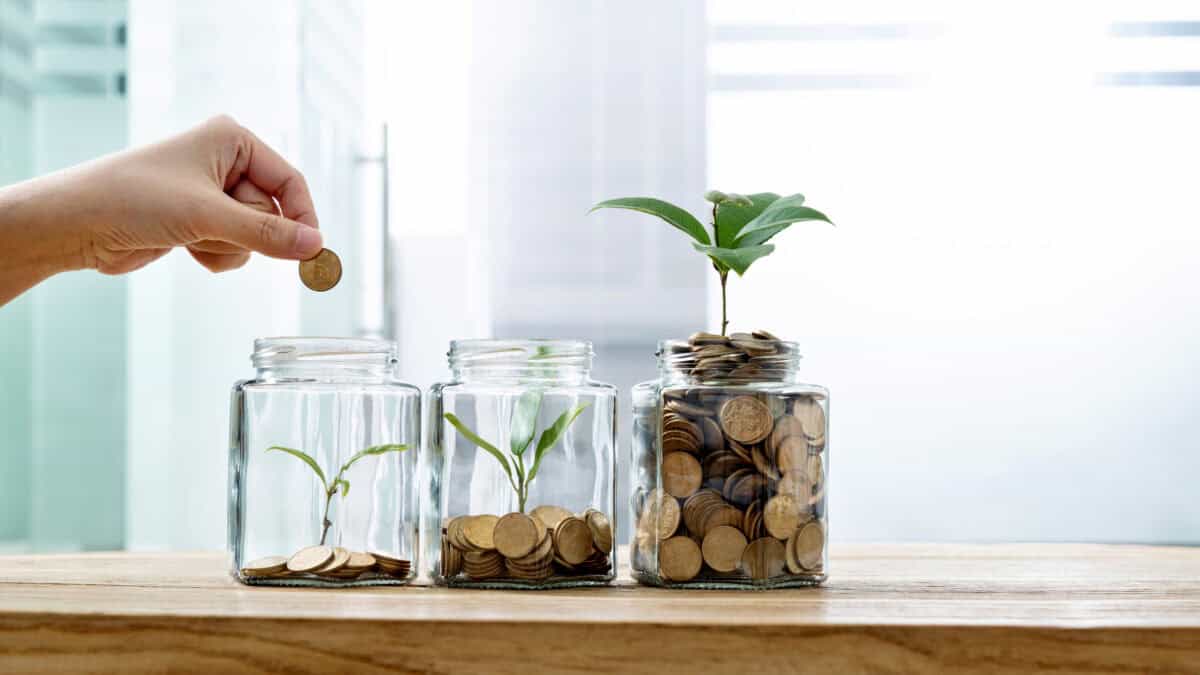 Ascending piles of coins and plants in three jars, with a hand putting a coin in the first jar.