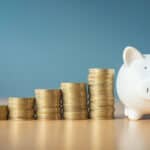 Rising stacks of coins next to a piggy bank.