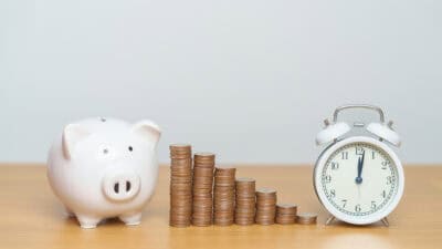 Coins in ascending order from left to right, with a piggy bank and clock on the sides.