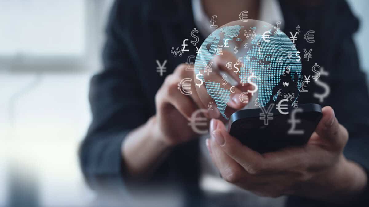 Woman using mobile phone for digital banking, with hologram of globe and different currency symbols.