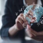 Woman using mobile phone for digital banking, with hologram of globe and different currency symbols.