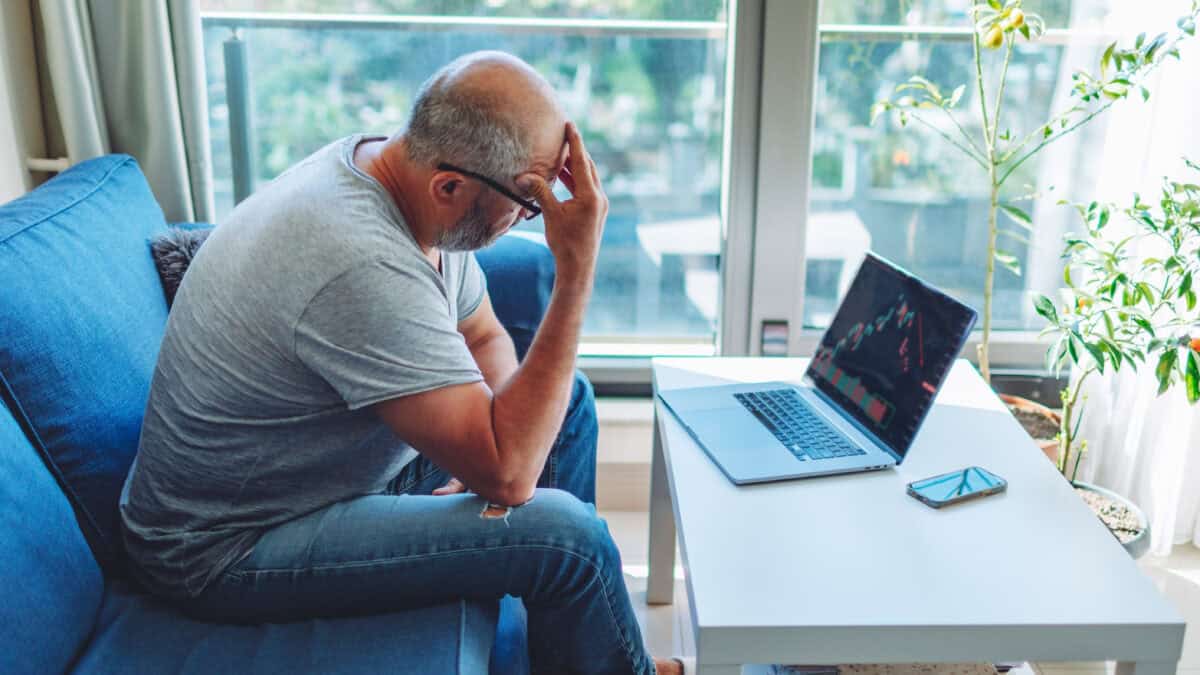 Disappointed man with his hand to his forehead, looking at a falling share price on his laptop.