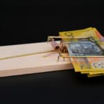 Rat trap with Australian $50 notes on black background.