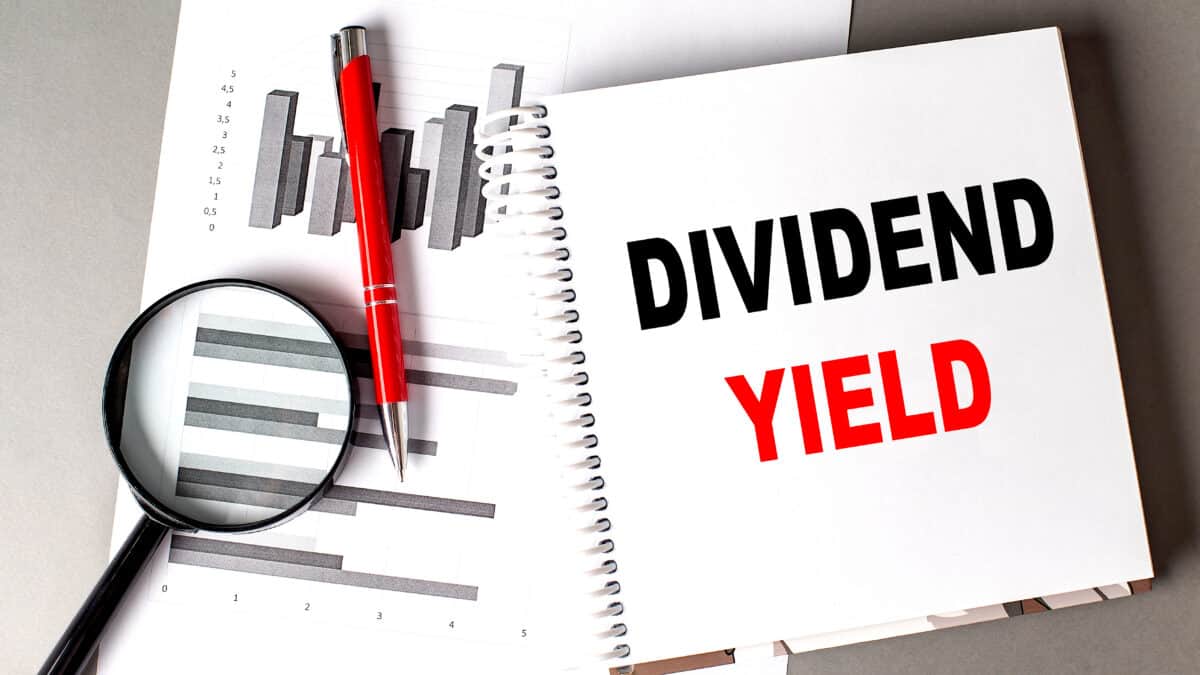Dividend yield written on a notebook with a chart, pen, and magnifying glass next to it.