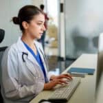 Doctor with stethoscope typing on her computer.