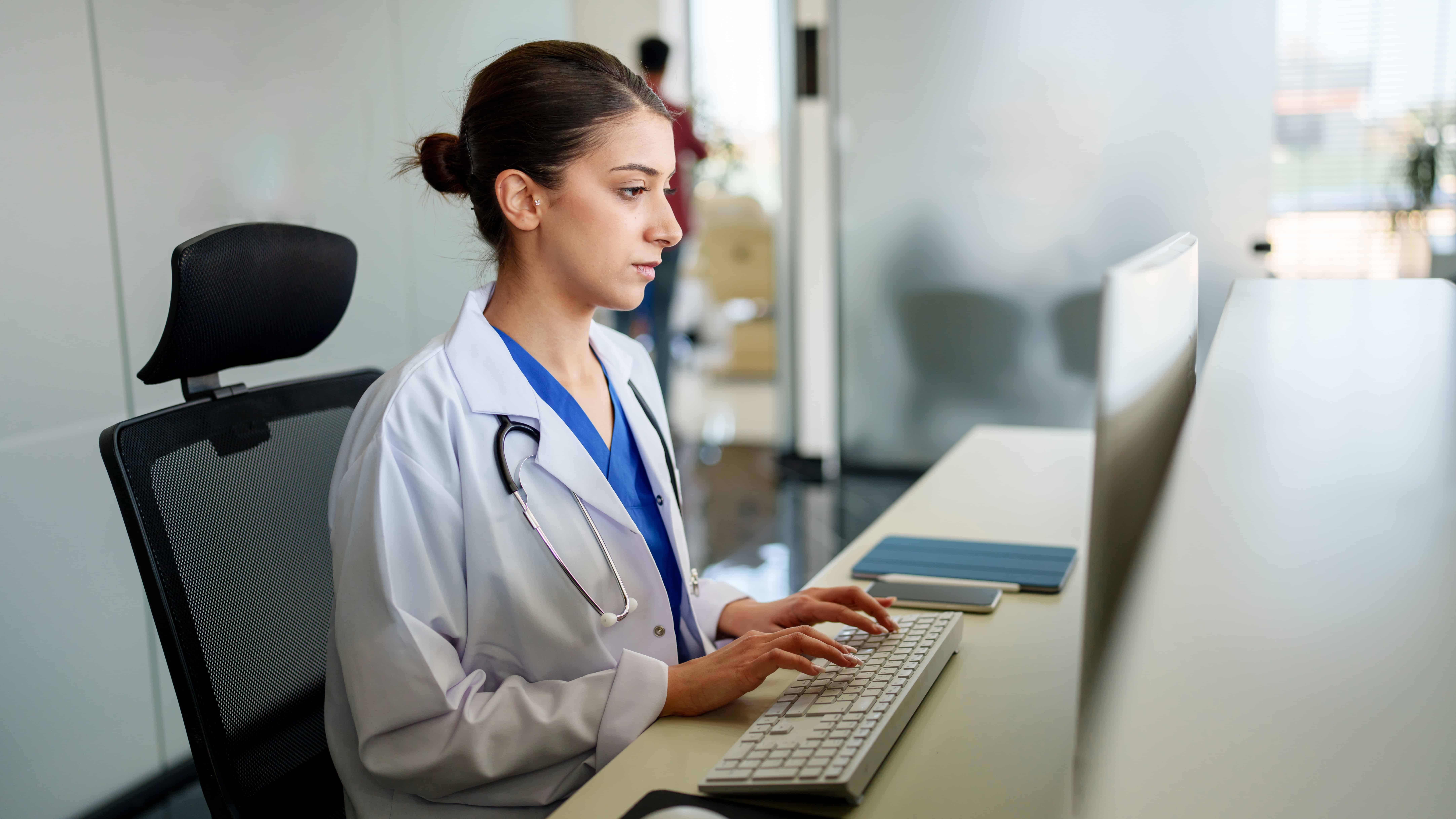 Doctor with stethoscope typing on her computer.