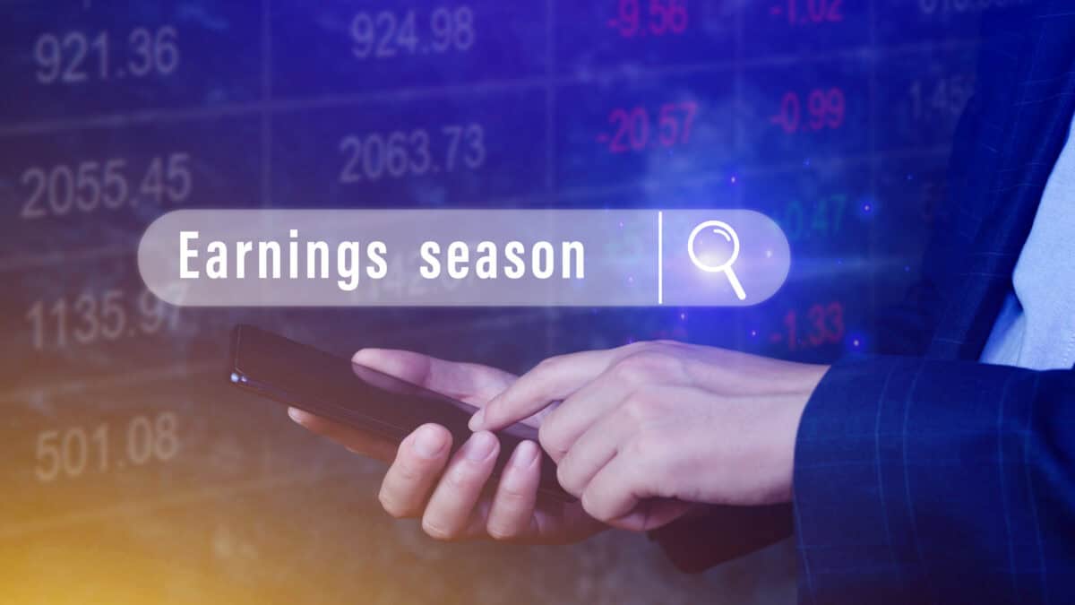 Hand touching smartphone with earnings season written in a search bubble above.