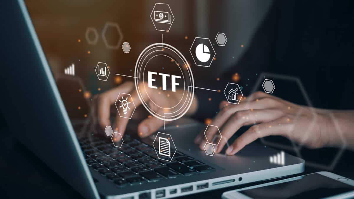 Person working on a computer with a hologram of the word ETF along with finance-related images.